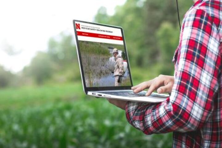 Student works on Pesticide Safety Education Program on a laptop in the middle of a field