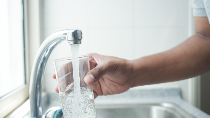 Hand filling a glass with water from a kitchen faucet.